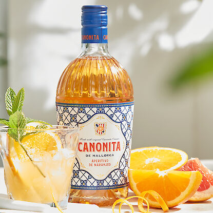 Bouteille d'apéritif Canonita avec un cocktail et des tranches d'orange fraîches sur une table.