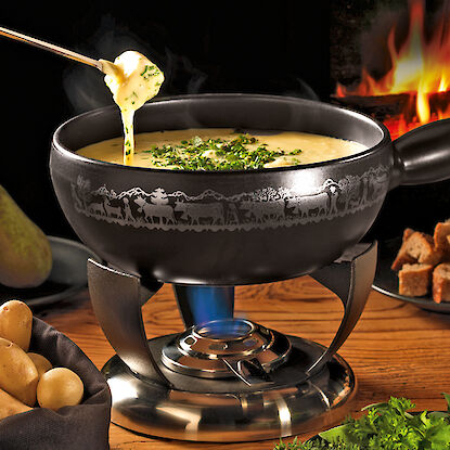 Fondue au fromage dans une casserole noire sur une table en bois devant un feu de cheminée.