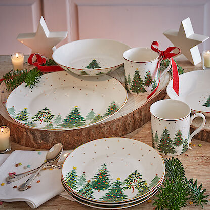 Vaisselle de Noël avec motif de sapin, décorée avec des bougies et des branches de sapin.