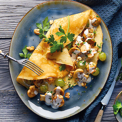 Crêpe farci aux champignons, raisins et sauce à la crème, servi sur une assiette bleue.