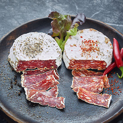 Salami mit Pfeffer- und Paprika-Kruste auf einem Teller, garniert mit Salat und roten Chilischoten.