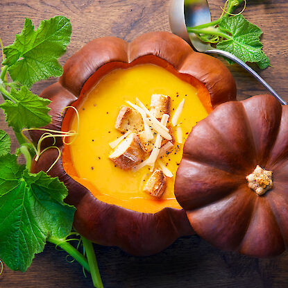 Soupe de potiron dans une citrouille évidée, garnie de pain et de fromage.