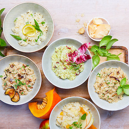 Cinq différents bols de risotto, décorés avec des ingrédients frais.