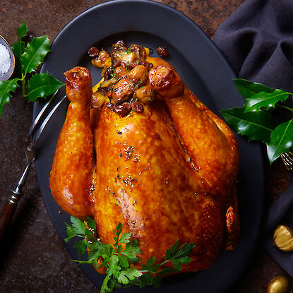 Oie de Noël rôtie dorée sur une assiette foncée, farcie aux marrons.