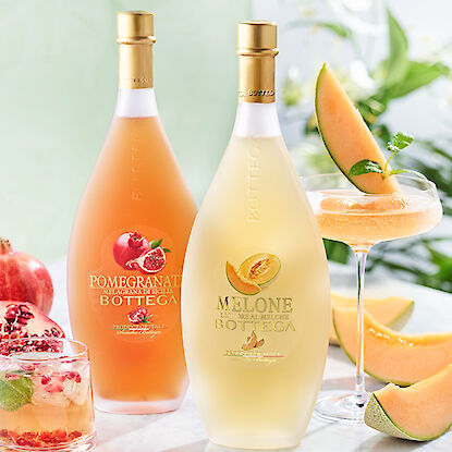 Bouteilles de liqueur de grenade et de melon Bottega avec des verres de cocktail garnis de fruits frais.