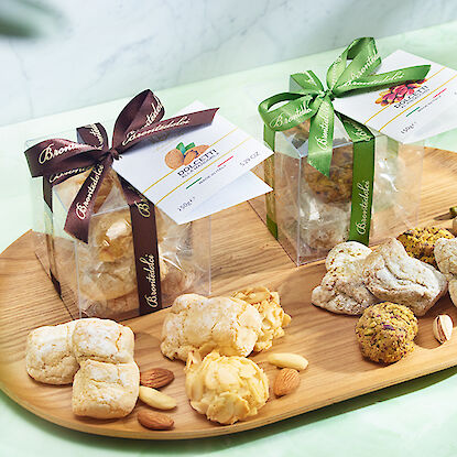 Assortiment de biscuits italiens artisanaux emballés avec des rubans, présentés sur un plateau en bois avec des amandes.