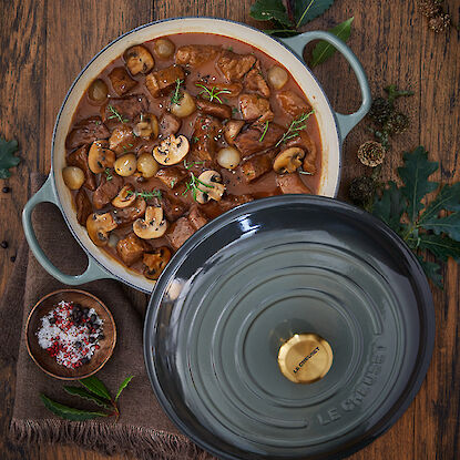 Le creuset gusseiserner Bräter mit einem Schmorgericht aus Fleisch, Zwiebeln und Pilzen