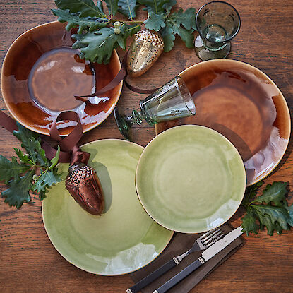 Rustikal gedeckter Tisch mit braunen und grünen Tellern.