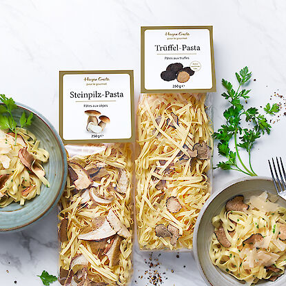 Steinpilz-Pasta und Trüffel-Pasta in Verpackungen, serviert auf Tellern mit frischen Kräutern.