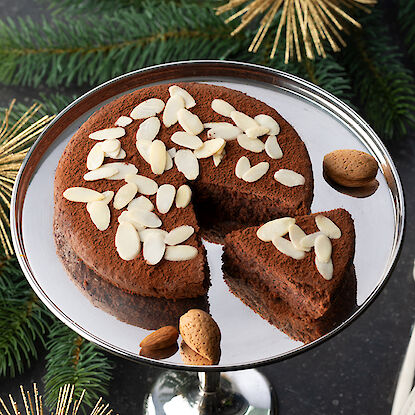 Schokoladenkuchen mit Mandelsplittern, weihnachtlich dekoriert mit goldenen Verzierungen.