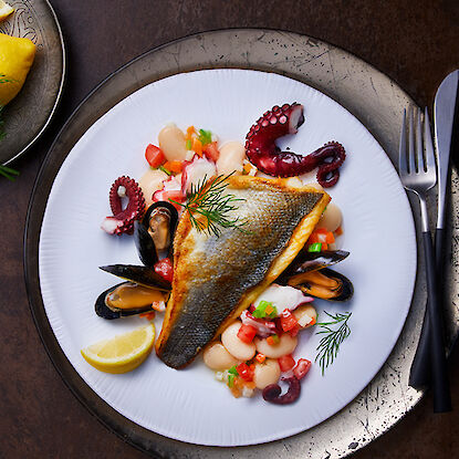 Gebratener Fischfilet serviert mit Oktopus, Muscheln, weißen Bohnen und Gemüse.