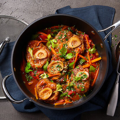 Ein Topf mit Osso Buco, garniert mit frischen Kräutern und Gemüse