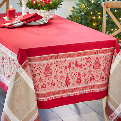 Weihnachtlich dekorierter Tisch mit roter Tischdecke, die mit Rentier- und Tannenbaum-Motiven