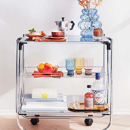 Chariot de service élégant avec des plateaux en verre, décoré de verres colorés.