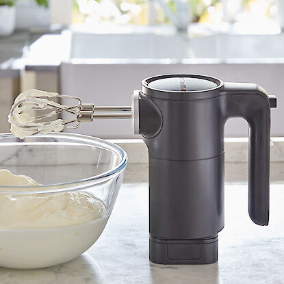 Mixeur à main KitchenAid noir avec de la crème dans un bol en verre sur un plan de travail de cuisine.