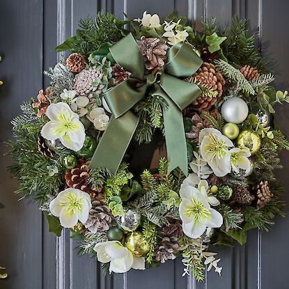 Weihnachtskranz mit weißen Blüten, Tannenzapfen, grünen Kugeln und einer großen Schleife