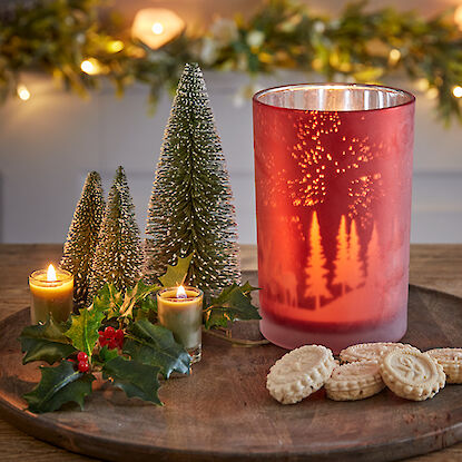 Festlich dekorierter Tisch mit Kerzen, Miniaturtannen, Weihnachtskeksen und einer roten Laterne