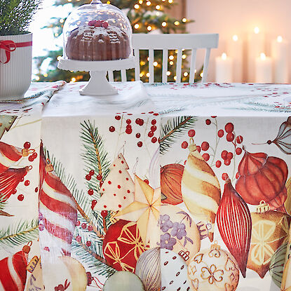 Ein festlich gedeckter Tisch mit weihnachtlicher Tischdecke, verziert mit Ornamenten