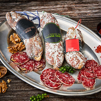 Variétés de saucissons sur un plateau en argent, accompagnées de noix et de poivre vert.