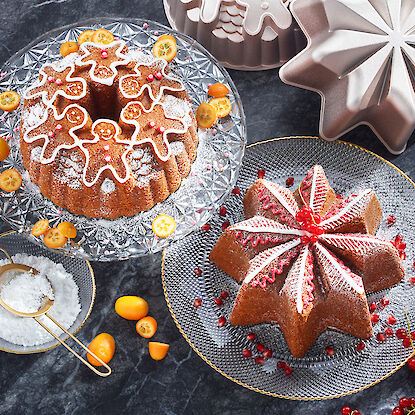 Deux gâteaux festifs en forme d'étoile et de couronne sur des assiettes en verre, entourés de sucre glace, de kumquats et de groseilles rouges.