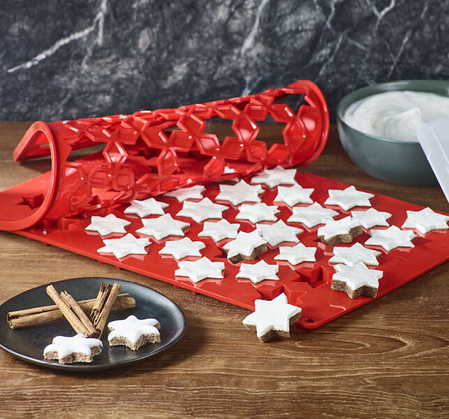 Moule rouge avec des étoiles à la cannelle, accompagné de bâtons de cannelle et d'un bol de glaçage au blanc d'œuf.