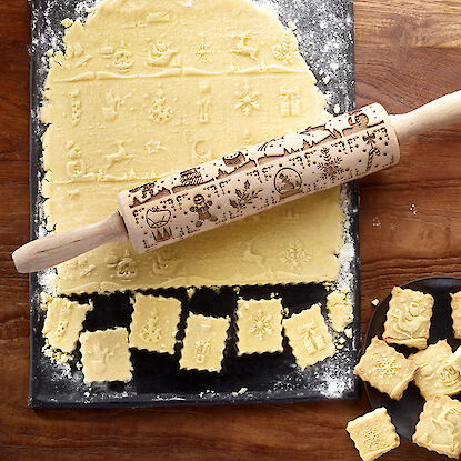 Pâte avec rouleau à pâtisserie gravé de motifs de Noël et biscuits découpés.