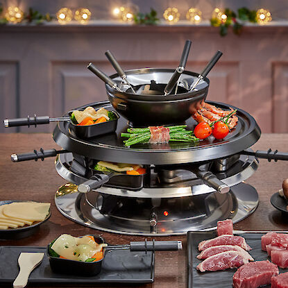 Raclette-Grill mit Fondue-Set, gefüllt mit Gemüse und Fleisch, umgeben von Beilagen.