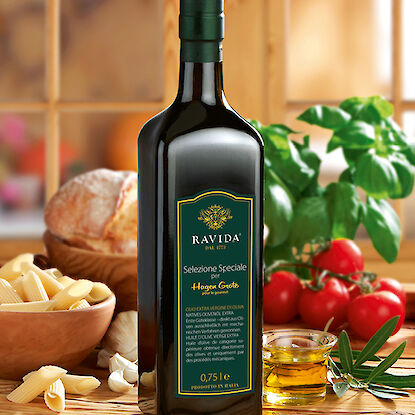 Flasche Hagen Grote RAVIDA Olivenöl umgeben von Pasta, Brot und frischen Tomaten.