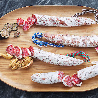 Différentes variétés de saucisson avec truffes, noix et oignons sur un plateau en bois.