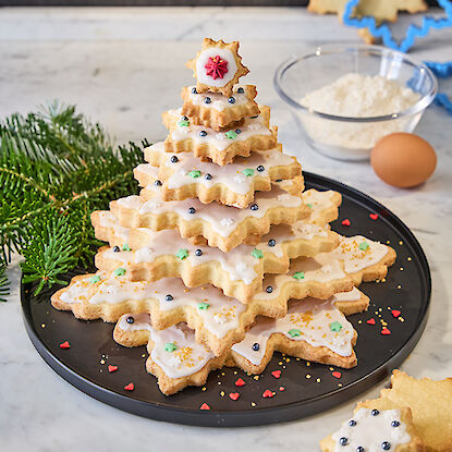 Weihnachtsbaum aus sternförmigen Keksen mit Zuckerguss und Perlendeko auf einem Teller.