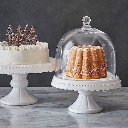 Zwei Kuchen auf Tortenständern, einer mit Glasglocke, der andere mit Schokodeko-Tannenbäumen.