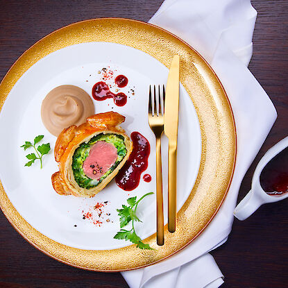 Festlich angerichtetes Filet Wellington mit roter Sauce, Püree und Blattdeko