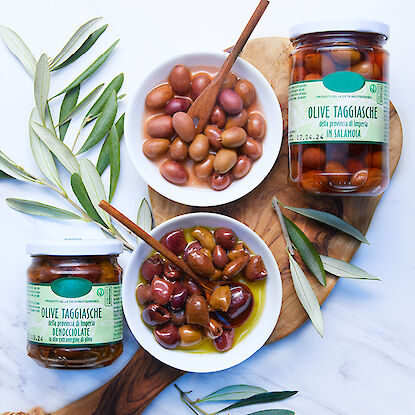 Olives Taggiasca en bocaux et dans des bols sur une planche en bois