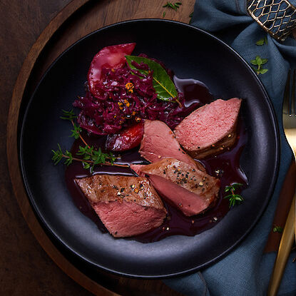 Viande de gibier tendre avec chou rouge et pomme, servie sur une assiette noire