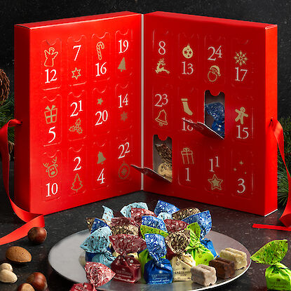 Adventskalender mit bunten Tartufi-Pralinen, festlich dekoriert auf einem Tisch mit Nüssen