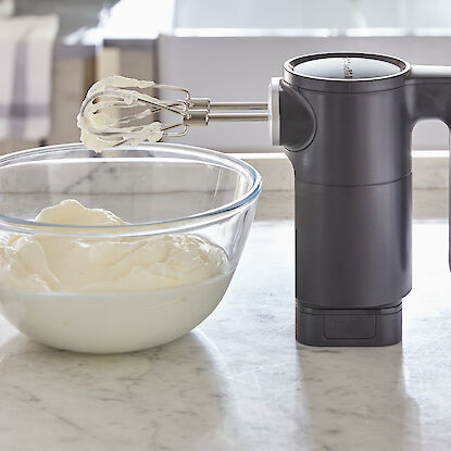 Fouet électrique avec crème fouettée dans un bol en verre, accompagné de fraises fraîches sur un plan de travail de cuisine.