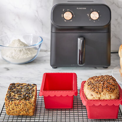 Brot in roten Silikonformen, geschnittenes Brot, Mehl und Küchenmaschine auf Marmorarbeitsplatte.