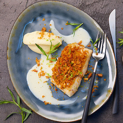 Fischfilet mit knuspriger Kruste, serviert mit Kartoffelpüree und Sauce auf einem dunkelblauen Teller.