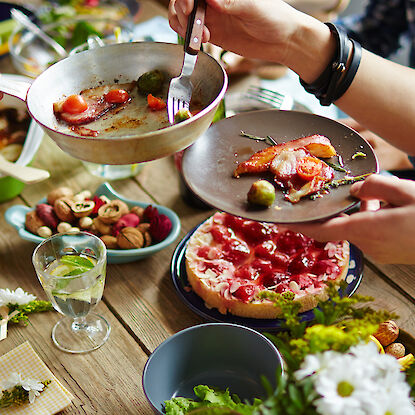 Table festive avec des plats salés et sucrés, boissons, fleurs et convives partageant un repas ensemble.