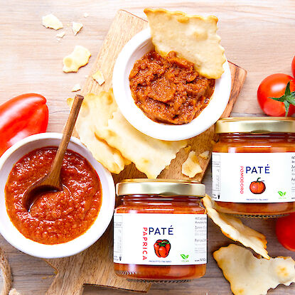 Paté aux poivrons et tomates en bocaux, avec crackers, tomates fraîches et poivron sur une planche en bois.