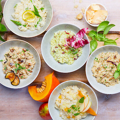 Cinq variétés de risotto dans des bols, décorés avec des ingrédients frais comme potiron, pomme, citron et herbes.