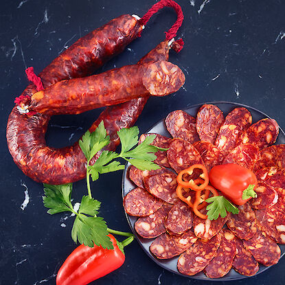 Saucisson chorizo entier et en tranches disposé sur une assiette, décoré de persil et de poivron rouge.