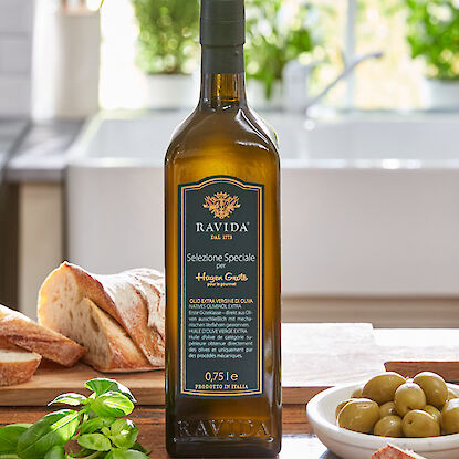 Huile d'olive Ravida avec pain, olives et basilic dans une cuisine lumineuse.