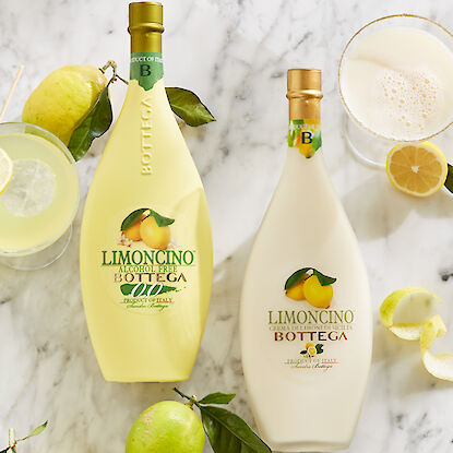 Deux bouteilles de Limoncino Bottega avec citrons et cocktails sur une table en marbre.