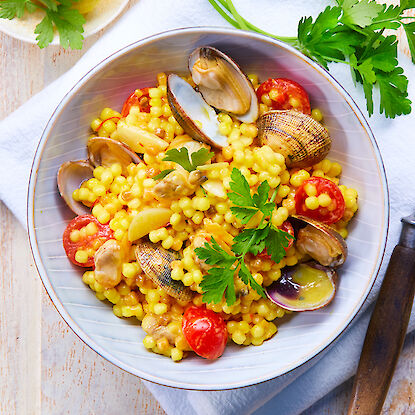 Couscous perlé aux palourdes, tomates cerises, herbes fraîches et citron, servi dans une assiette blanche.