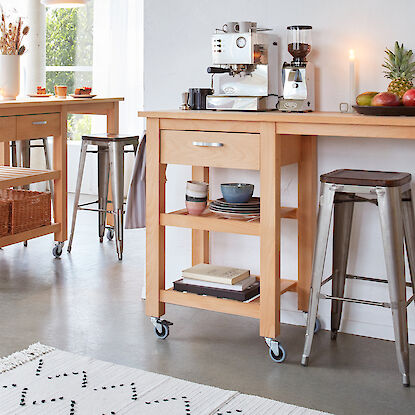 Holz-Kücheninseln auf Rollen mit Metallhockern, Kaffeemaschine, Obstschale und Dekoration in einer modernen Küche.