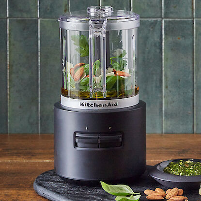 Kompakte KitchenAid Küchenmaschine mit Zutaten für frisches Pesto auf einem Servierbrett.