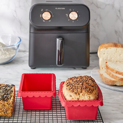 Brot in roten Silikonformen, geschnittenes Brot, Mehl und Küchenmaschine auf Marmorarbeitsplatte.