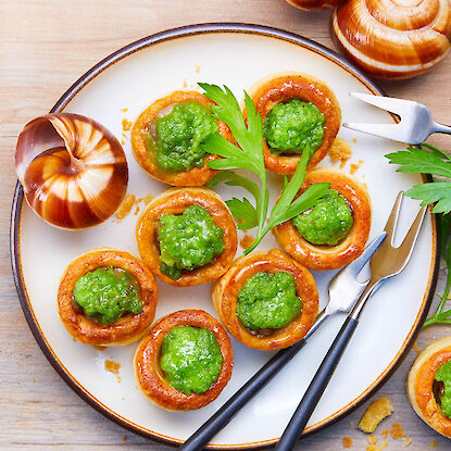 Französische Escargots in Blätterteig mit Kräuterbutter, serviert auf Teller mit Petersilie.