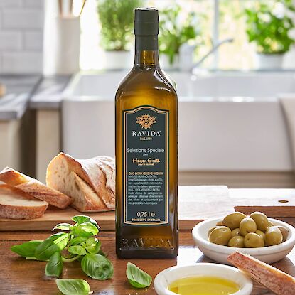 Huile d'olive exclusive Hagen Grote de Ravida avec pain, olives et basilic sur une table en bois rustique.